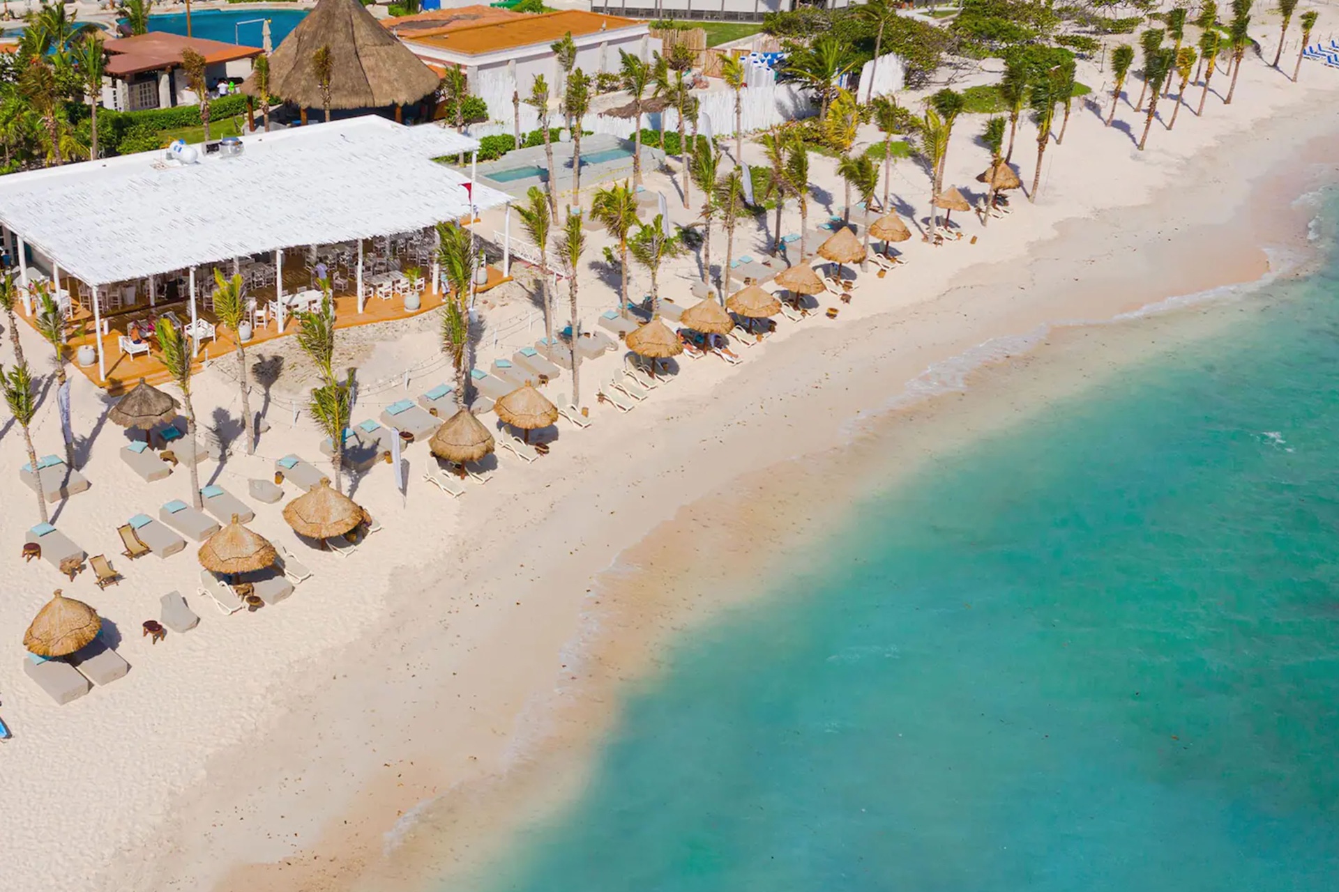 Aerial view of Kay Beach Club with beach loungers, palm palapas and turquoise water